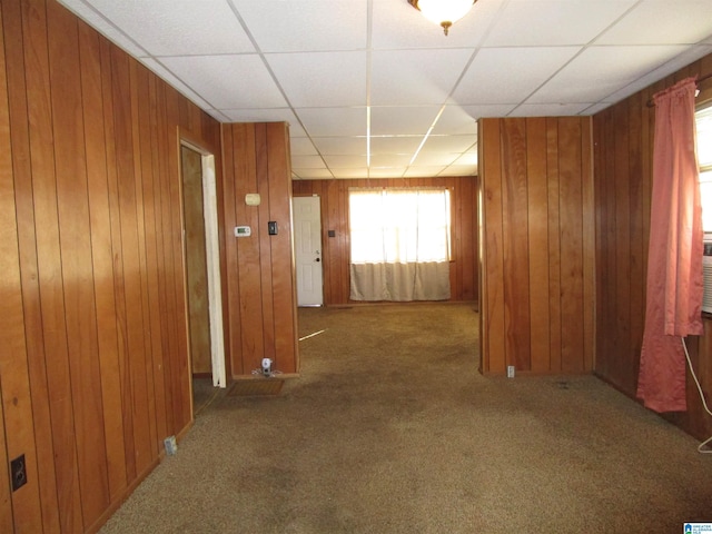 corridor with carpet floors, wood walls, and a paneled ceiling