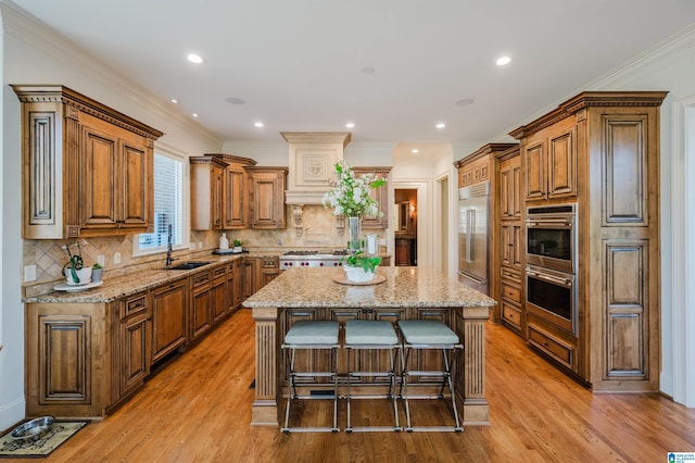 kitchen with brown cabinetry, a kitchen island, light stone counters, stainless steel appliances, and a sink