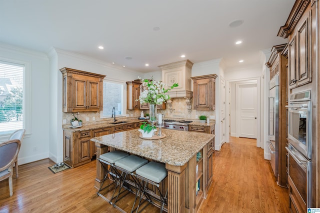 kitchen with brown cabinetry, a breakfast bar, crown molding, light wood-type flooring, and a sink