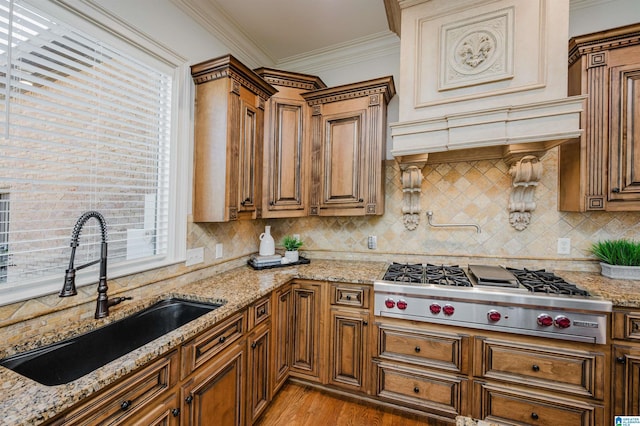 kitchen with stainless steel gas cooktop, a sink, ornamental molding, light wood-type flooring, and brown cabinetry