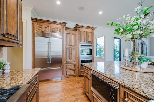 kitchen featuring light wood finished floors, light stone counters, crown molding, and built in appliances