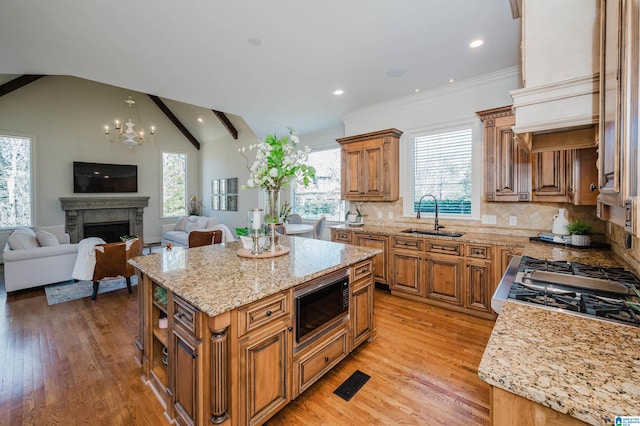 kitchen featuring lofted ceiling, built in microwave, a sink, light stone countertops, and brown cabinetry