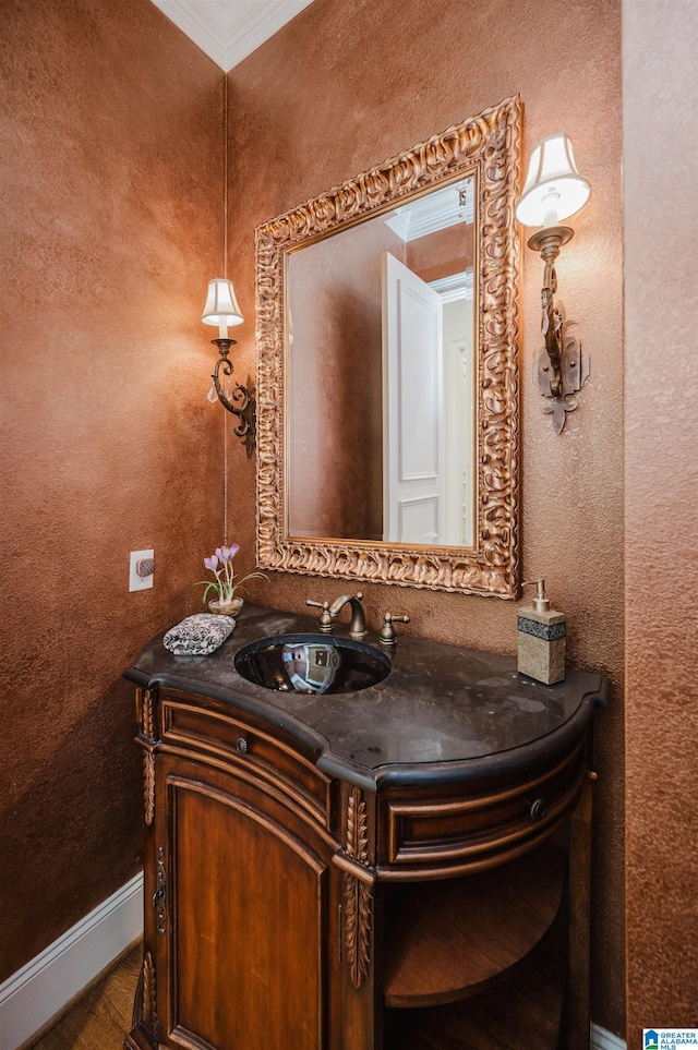 bathroom with a textured wall, baseboards, ornamental molding, and vanity