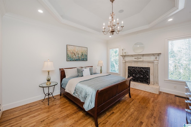 bedroom with a premium fireplace, ornamental molding, a raised ceiling, and wood finished floors