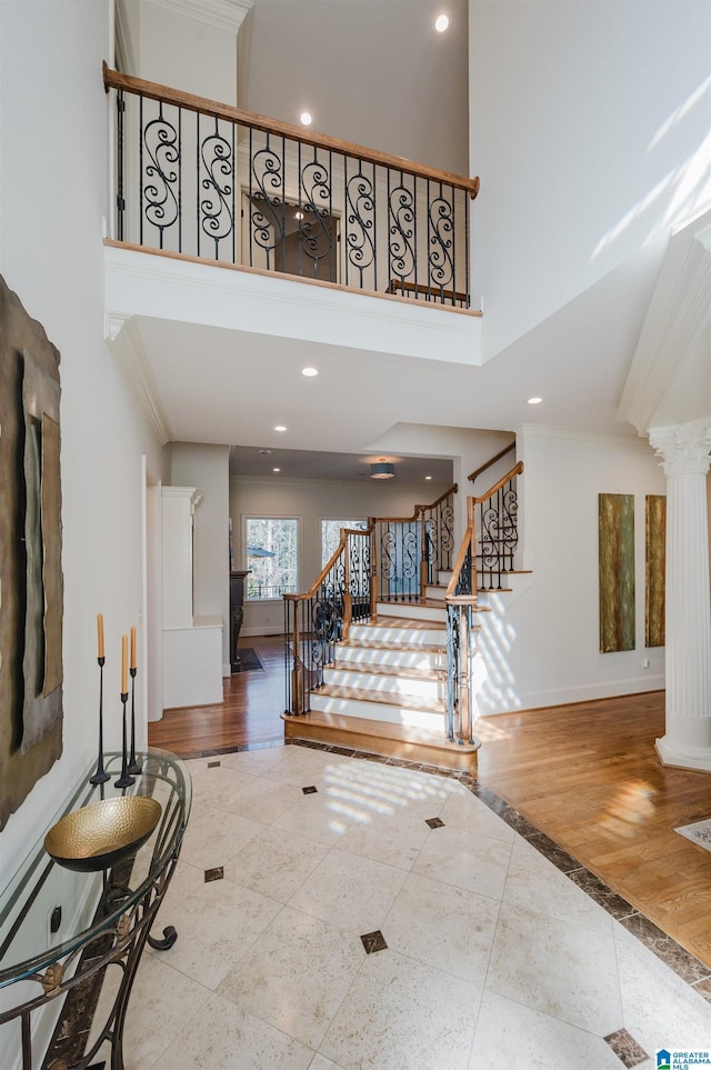 foyer with a high ceiling, wood finished floors, baseboards, stairs, and ornate columns