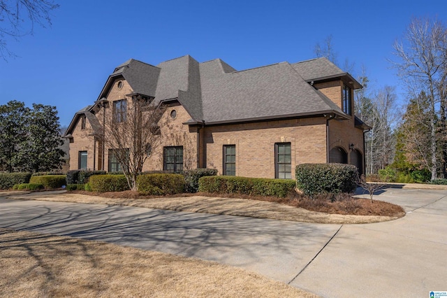 exterior space featuring an attached garage, a shingled roof, concrete driveway, and brick siding