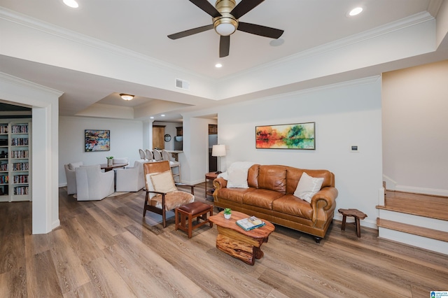 living room featuring visible vents, a raised ceiling, ornamental molding, wood finished floors, and stairs