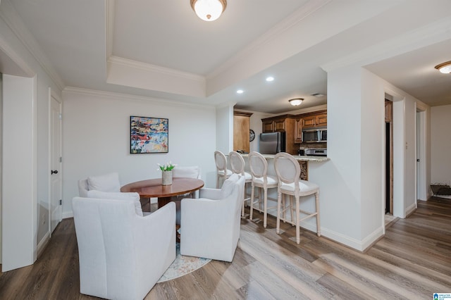 dining area with ornamental molding, a raised ceiling, baseboards, and wood finished floors