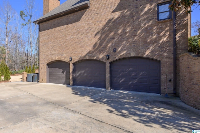 view of property exterior featuring a garage, a chimney, concrete driveway, and brick siding