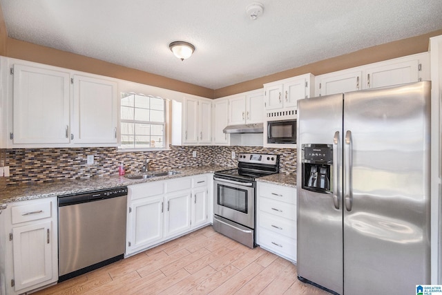 kitchen featuring light stone counters, stainless steel appliances, white cabinetry, a sink, and under cabinet range hood