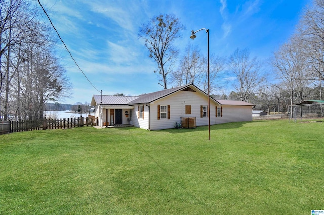 rear view of house featuring a yard, metal roof, and fence