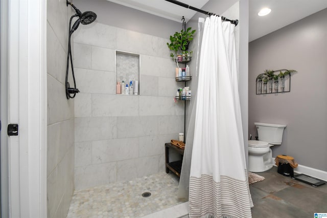 bathroom with toilet, baseboards, and tiled shower