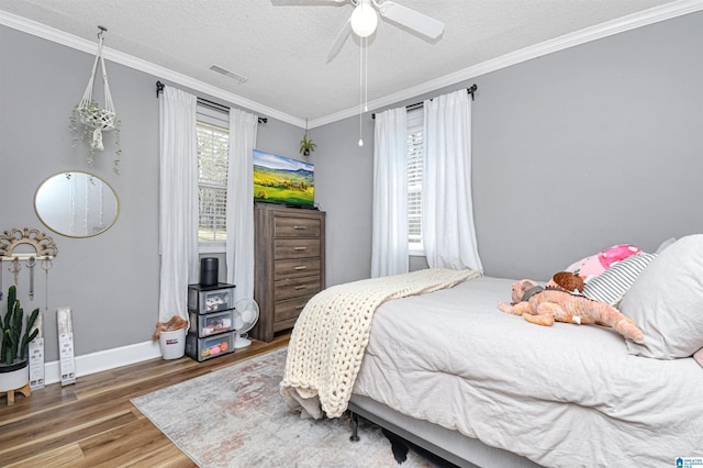 bedroom with a textured ceiling, wood finished floors, visible vents, baseboards, and ornamental molding