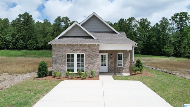 view of front of property featuring brick siding, roof with shingles, and a front lawn