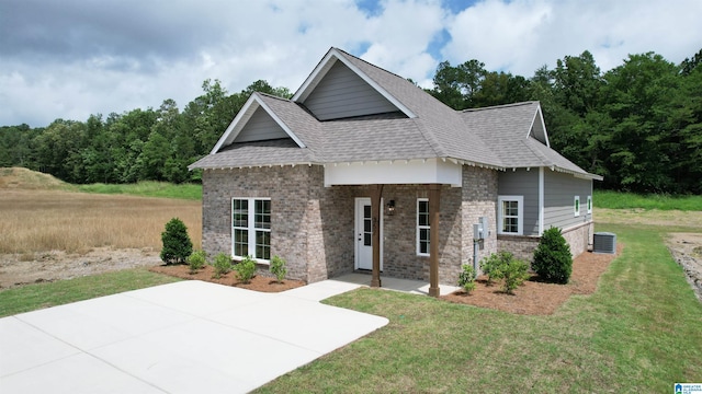 view of front facade featuring roof with shingles, a patio, brick siding, central air condition unit, and a front lawn