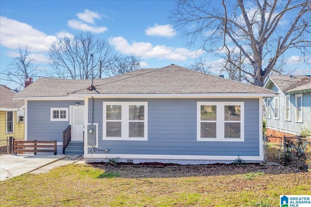 view of front of property featuring entry steps, fence, a front lawn, and roof with shingles