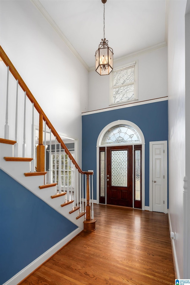 foyer featuring ornamental molding, wood finished floors, a towering ceiling, and baseboards