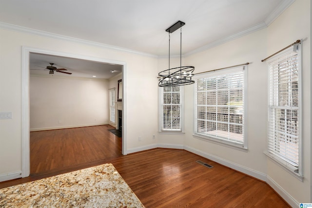 unfurnished dining area featuring ornamental molding, baseboards, a fireplace with flush hearth, and wood finished floors