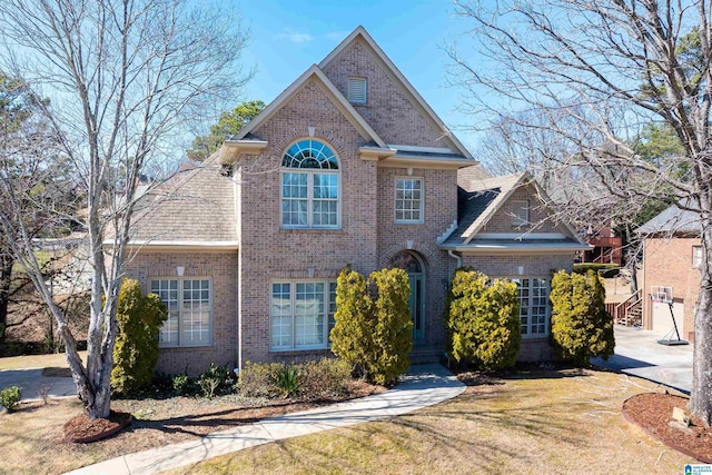 traditional home featuring brick siding, a front lawn, and roof with shingles