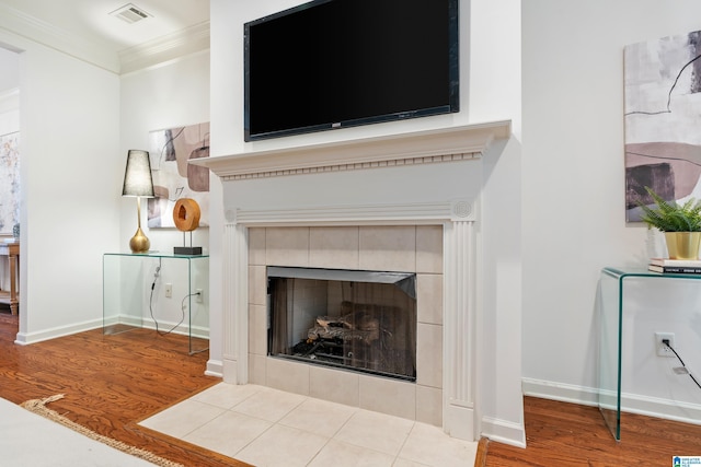 interior details with baseboards, visible vents, a tiled fireplace, ornamental molding, and wood finished floors