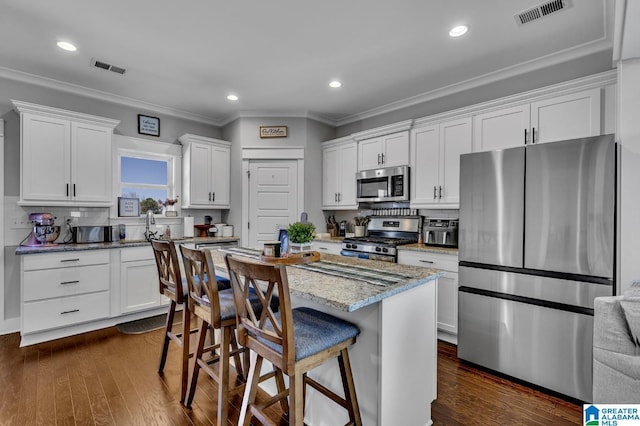 kitchen featuring visible vents, a kitchen island, appliances with stainless steel finishes, light stone countertops, and white cabinetry