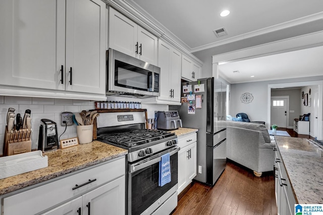 kitchen featuring light stone counters, white cabinets, open floor plan, appliances with stainless steel finishes, and crown molding