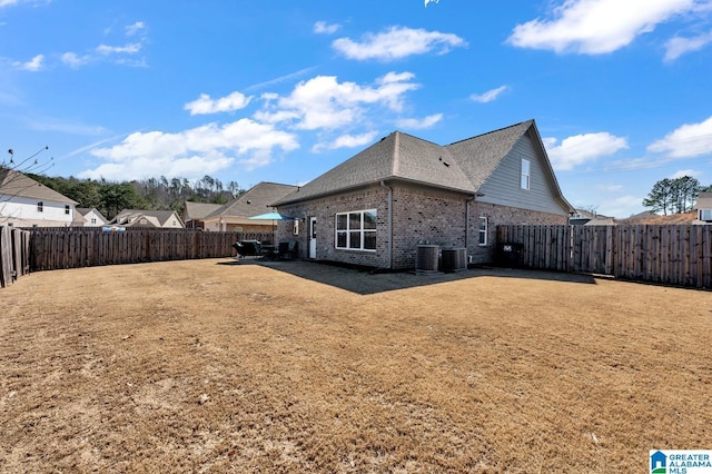 rear view of house with central AC unit, a fenced backyard, and brick siding