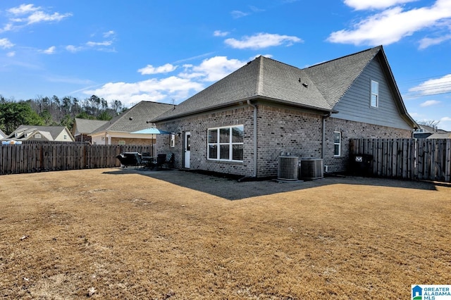 rear view of property featuring a shingled roof, a fenced backyard, a patio, and central AC unit