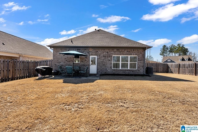 back of house featuring a fenced backyard, cooling unit, brick siding, roof with shingles, and a lawn