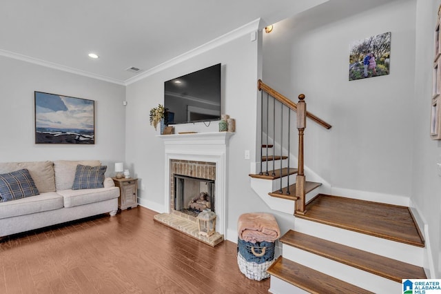 living room with wood finished floors, baseboards, stairs, ornamental molding, and a brick fireplace