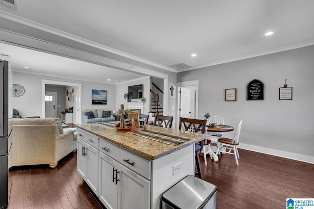 kitchen with a center island, visible vents, open floor plan, white cabinetry, and light stone countertops