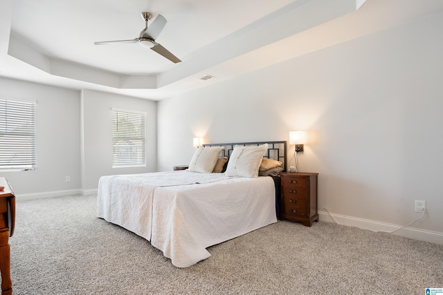 carpeted bedroom with a raised ceiling, visible vents, baseboards, and ceiling fan