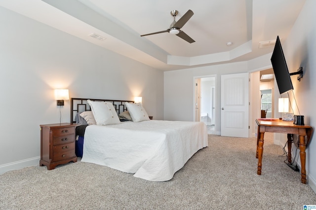 carpeted bedroom featuring a tray ceiling, visible vents, baseboards, and a ceiling fan