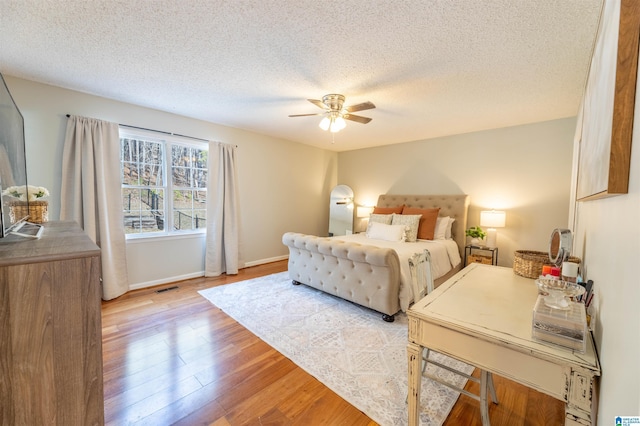 bedroom with visible vents, a ceiling fan, a textured ceiling, light wood-type flooring, and baseboards