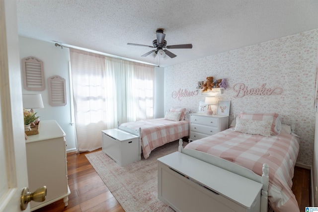 bedroom featuring a textured ceiling, ceiling fan, wood finished floors, and wallpapered walls