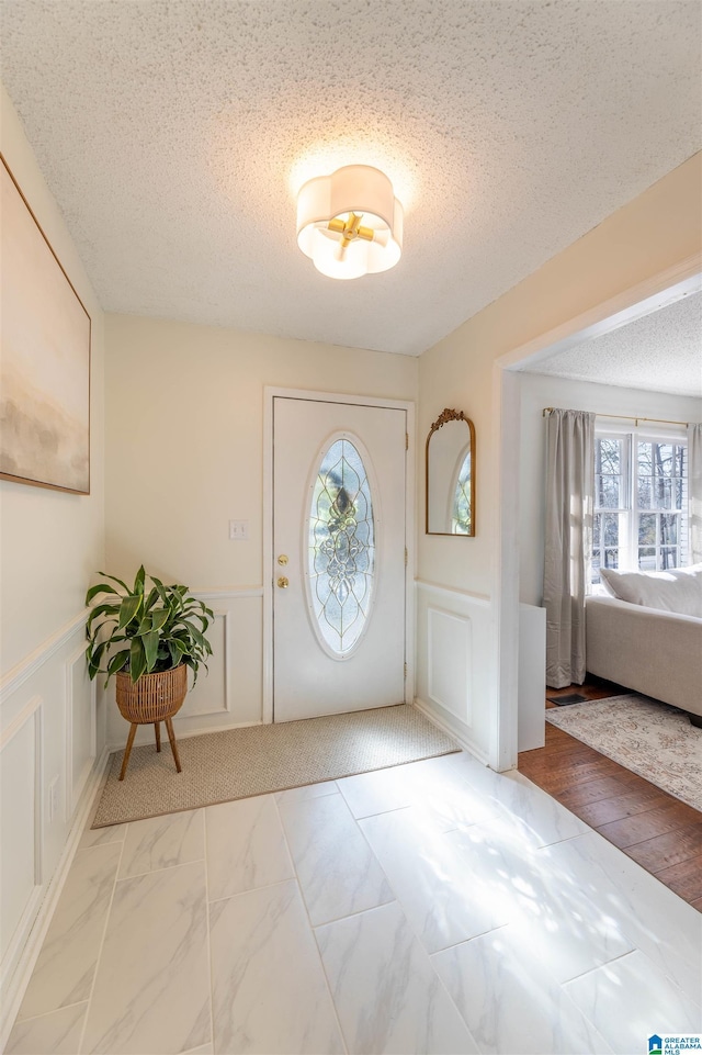 foyer entrance featuring marble finish floor, a wainscoted wall, a decorative wall, and a textured ceiling