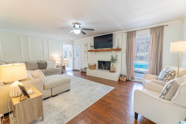 living room with a decorative wall, a fireplace, wood finished floors, a ceiling fan, and crown molding