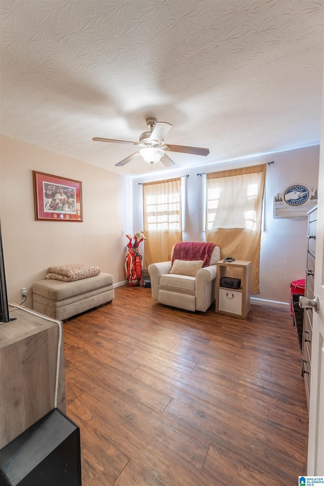 living area with ceiling fan, a textured ceiling, dark wood finished floors, and baseboards