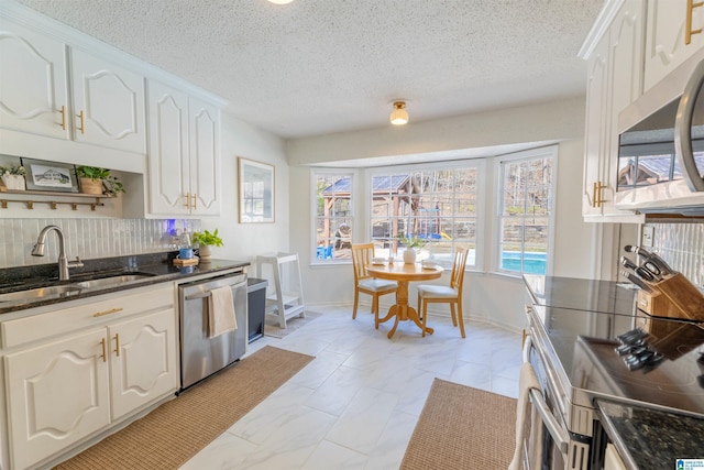 kitchen with white cabinets, dark stone countertops, stainless steel appliances, and a sink