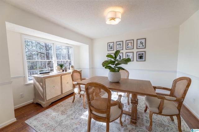 dining space featuring a textured ceiling, baseboards, and wood finished floors