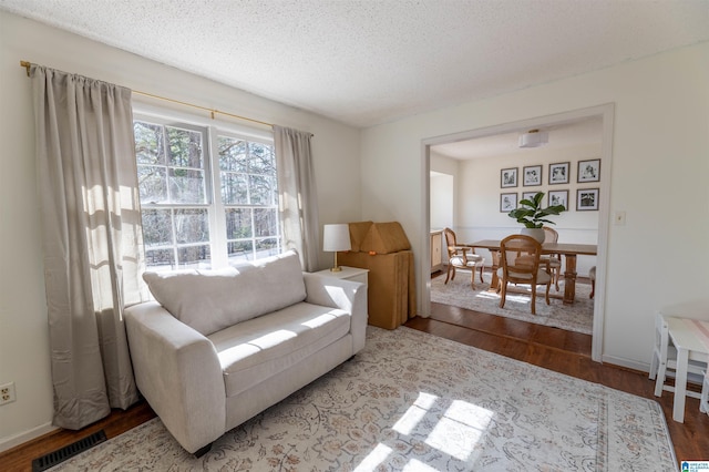 living room featuring a textured ceiling, wood finished floors, visible vents, and baseboards