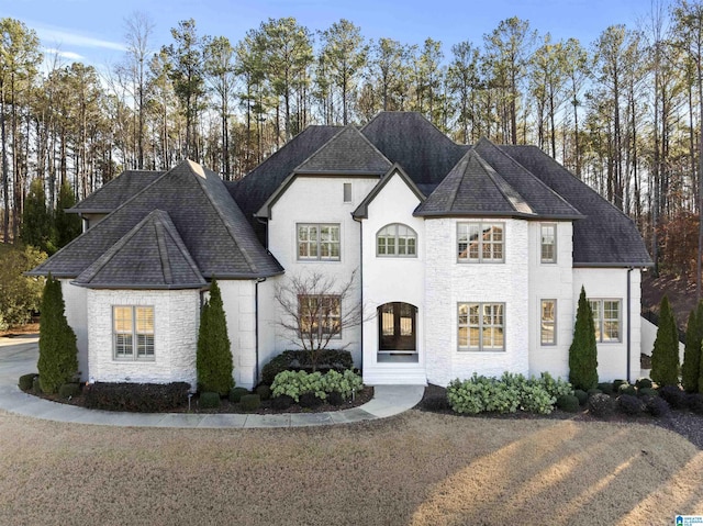 french country home featuring stone siding and a shingled roof