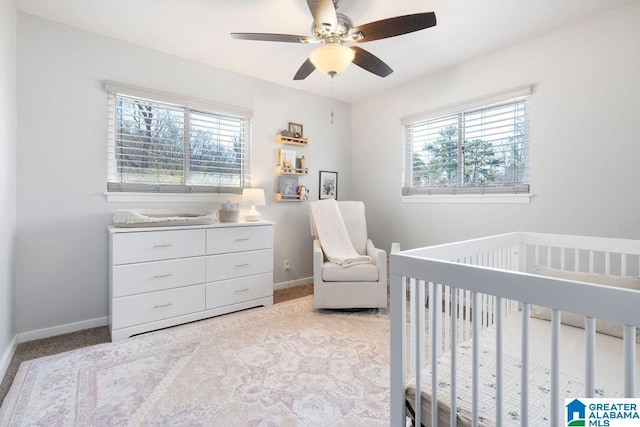 bedroom featuring a crib, a ceiling fan, light colored carpet, and baseboards