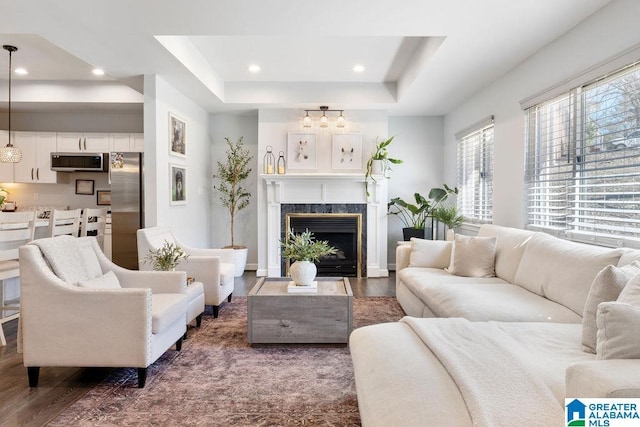 living area featuring recessed lighting, wood finished floors, a high end fireplace, baseboards, and a tray ceiling