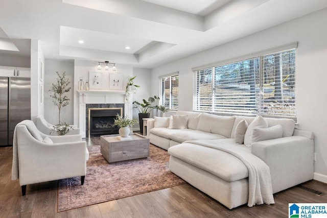 living area with recessed lighting, a premium fireplace, wood finished floors, baseboards, and a tray ceiling