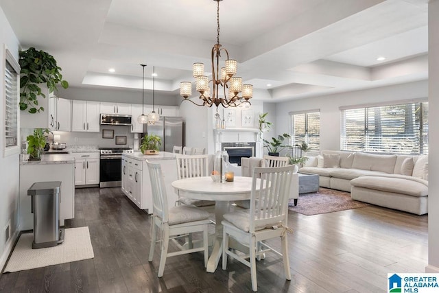 dining space featuring dark wood-style floors, recessed lighting, a raised ceiling, and a fireplace