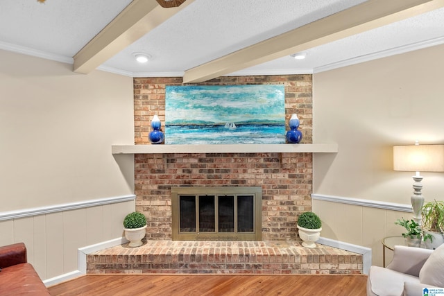 living room featuring a wainscoted wall, a textured ceiling, a fireplace, and beam ceiling