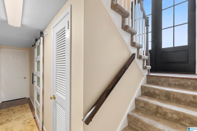 staircase featuring a barn door, a textured ceiling, and wood finished floors