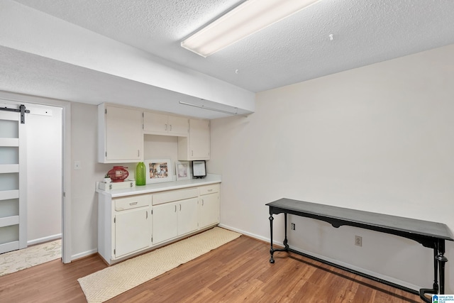 kitchen featuring light countertops, a barn door, light wood-style floors, a textured ceiling, and baseboards