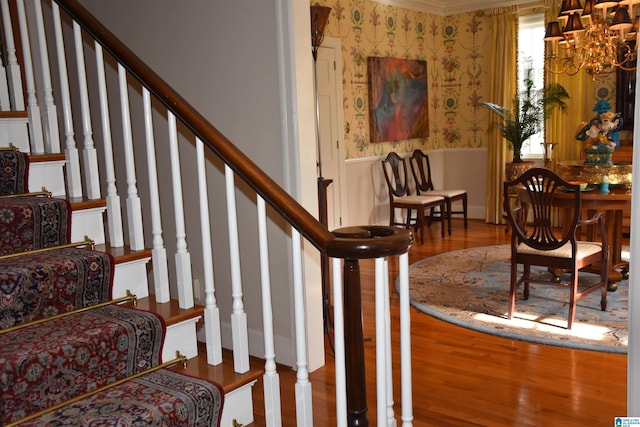 staircase featuring a notable chandelier, wainscoting, wood finished floors, and wallpapered walls